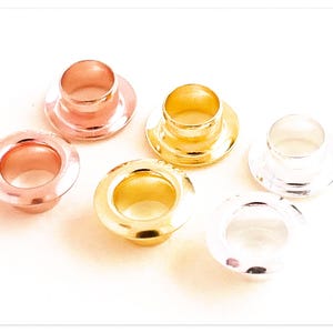 May include: Six metal eyelets in different colors: gold, silver, and rose gold. The eyelets are round and have a raised lip around the edge.