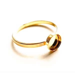 Op de afbeelding: Een gouden ring met een ronde bezel-setting voor een cabochon-steen. De ring is simpel en elegant, perfect om een ​​toets van glans toe te voegen aan elke outfit.