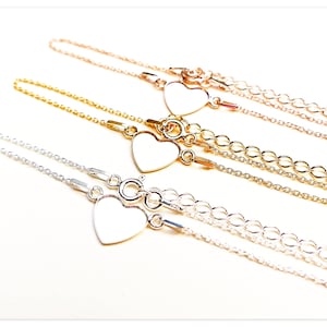 Könnte beinhalten: Drei zarte herzförmige Armbänder in Silber, Gold und Roségold. Jedes Armband hat einen kleinen, leeren Herzanhänger und eine zarte Kette.