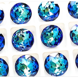 Può includere: Dodici perline rotonde in vetro blu e verde iridescente con un foro nella parte superiore per l'infilaggio. Le perline sono disposte in un motivo a griglia su una superficie bianca.