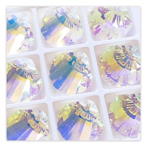 May include: A close-up of a set of iridescent crystal beads in a white gridded display box. The beads are faceted and have a rainbow sheen.