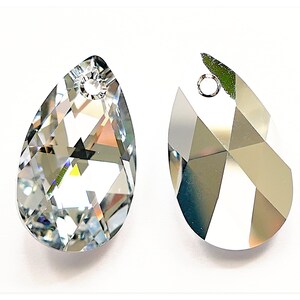 Puede incluir: Dos colgantes de cristal transparente facetados en forma de l&aacute;grima, con un agujero en la parte superior para ensartar. Los cristales est&aacute;n tallados con m&uacute;ltiples facetas, que reflejan la luz. Sobre fondo blanco.
