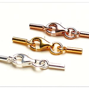 Könnte beinhalten: Drei Schmuckverschlüsse, einer silber, einer gold und einer roségold. Jeder Verschluss hat an einem Ende ein kleines Rohr und am anderen Ende einen Karabinerhaken.