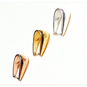 Könnte beinhalten: Drei Anhängerösen in verschiedenen Metalloberflächen: Silber, Gold und Roségold. Jede Öse hat ein einfaches U-förmiges Design.