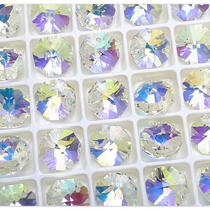 May include: A close-up view of a white plastic container filled with clear iridescent glass octagon-shaped beads. The beads have a rainbow effect and are arranged in rows.