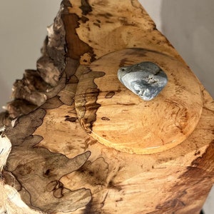 Op de afbeelding: Een houten doos met een natuurlijk houtnerfpatroon en een grijze steen op de deksel.