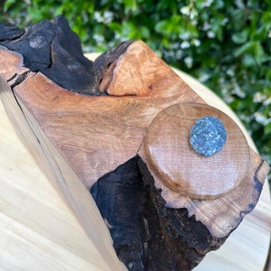 May include: A wooden sculpture with a natural wood finish and a dark brown stain. The sculpture has a circular indentation with a small, gray stone in the center.