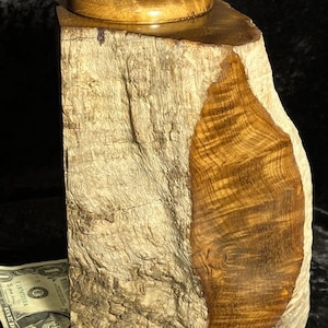 May include: A handcrafted wooden box with a natural, rustic aesthetic. The box features a light-colored, textured exterior with a contrasting, polished wood grain section. A small stone sits atop the lid, adding a unique touch. The box is approximately 6 inches tall.