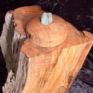May include: A wooden box with a lid, made from a tree trunk, with a green stone on top of the lid.