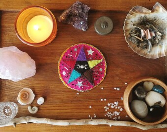 May include: A wooden tray with a variety of items for a spiritual ritual, including a pink rose quartz, a candle, a seashell, a bowl of stones, a stick, salt, and a five-pointed star with the symbol "30C" in the center.