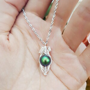 May include: A silver chain necklace with a green iridescent pearl pendant. The pearl is encased in a silver wire cage.