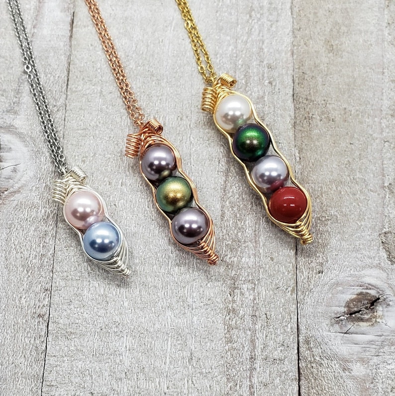 May include: Three necklaces with pea pod pendants. Each pendant features three pearls in different colors, including white, green, red, blue, and gray.