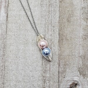 May include: A silver chain necklace with a silver wire wrapped pendant featuring two pearls, one pink and one blue.