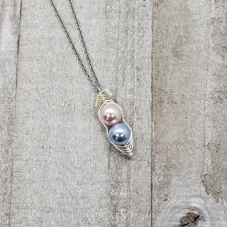 May include: A silver chain necklace with a silver wire wrapped pendant featuring two pearls, one pink and one blue.
