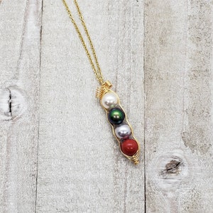 May include: A gold necklace with a pea pod charm. The charm has four pearls inside: white, green, white, and red.