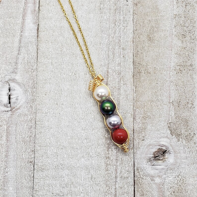 May include: A gold necklace with a pea pod charm. The charm has four pearls inside: white, green, white, and red.