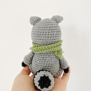 May include: A gray crocheted raccoon with a green scarf and a black and white tail.