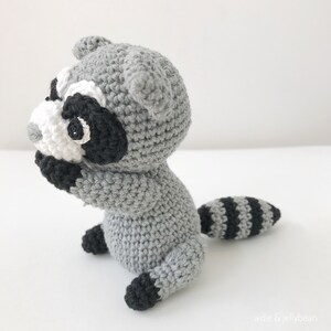 May include: A crocheted raccoon amigurumi toy with a gray body, black and white face, and a black and gray striped tail.