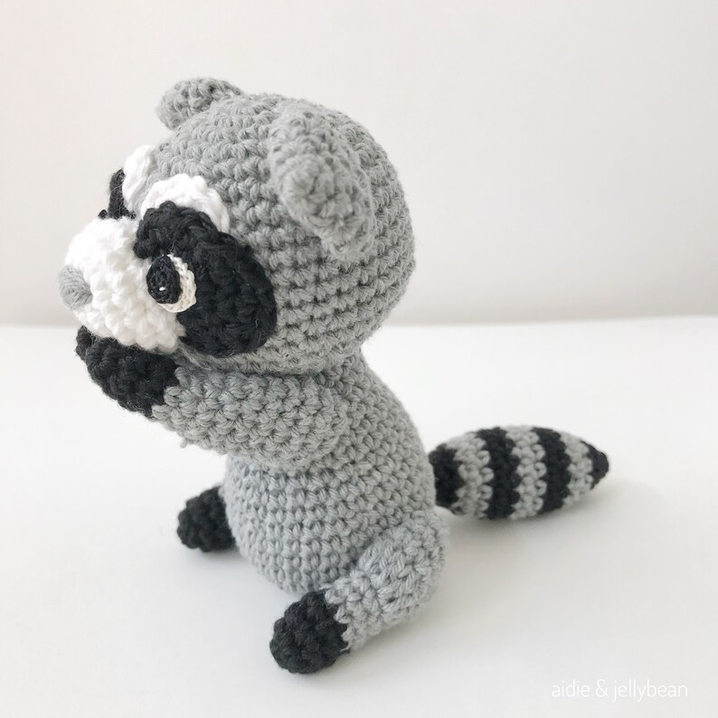 May include: A crocheted raccoon amigurumi toy with a gray body, black and white face, and a black and gray striped tail.