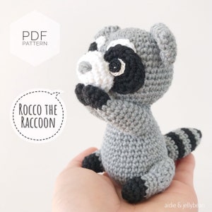 May include: Crochet pattern for Rocco the Raccoon, a gray crocheted stuffed animal with black and white facial features. The pattern is available as a PDF download.