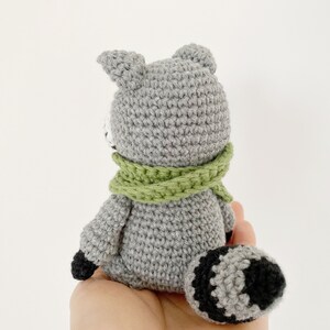 May include: A gray crocheted raccoon with a green scarf and a black and gray tail.