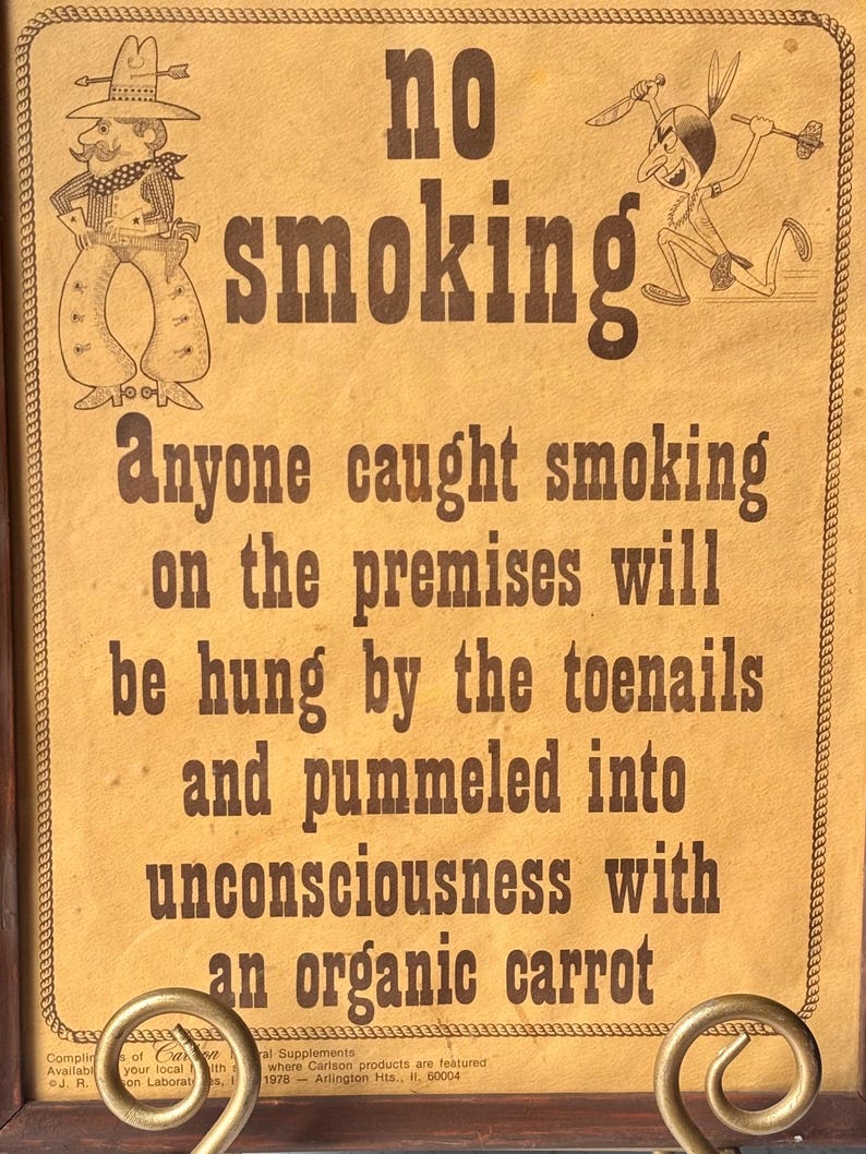 May include: A vintage-style sign with the words "no smoking" in large, bold letters. The sign features cartoon illustrations of a cowboy and a Native American. The text below warns of consequences for smoking on the premises.