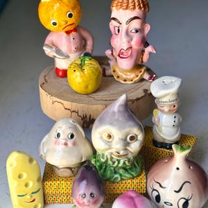 Puede incluir: Una colección de saleros y pimenteros de cerámica vintage con forma de varias frutas y verduras. El juego incluye un chef, una cebolla, un nabo, una seta, una cuña de queso y un melocotón. Los saleros son de colores brillantes y tienen rasgos faciales caprichosos.