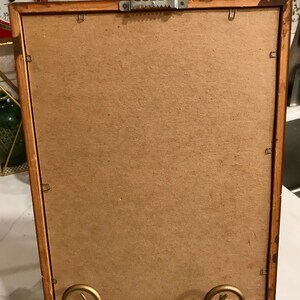May include: A rectangular wooden picture frame with a cardboard backing. The frame is supported by a gold-colored metal stand. The back of the frame has a sawtooth hanger for wall mounting.