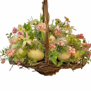 May include: A wicker basket filled with faux pastel pink and green flowers and speckled eggs. The basket has a brown woven handle.