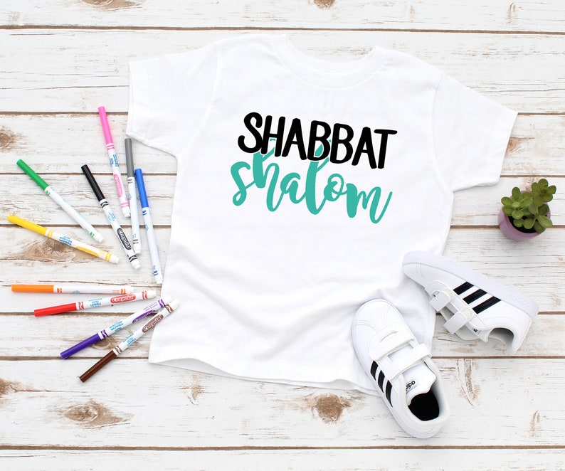 May include: White t-shirt with black and teal blue text that says "Shabbat Shalom".