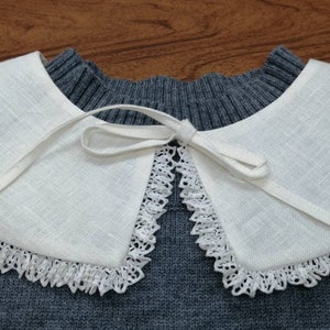 May include: A white linen collar with a lace trim and a white ribbon tied in a bow at the centre.