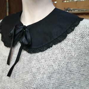 May include: A white knitted sweater with a black lace trim collar and a black satin bow tie.