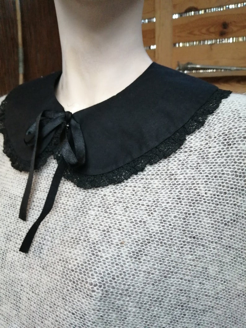 May include: A white knitted sweater with a black lace trim collar and a black satin bow tie.