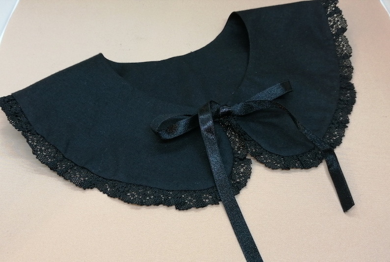 May include: A black fabric collar with a lace trim and a black satin ribbon tie. The collar is a fashion accessory.