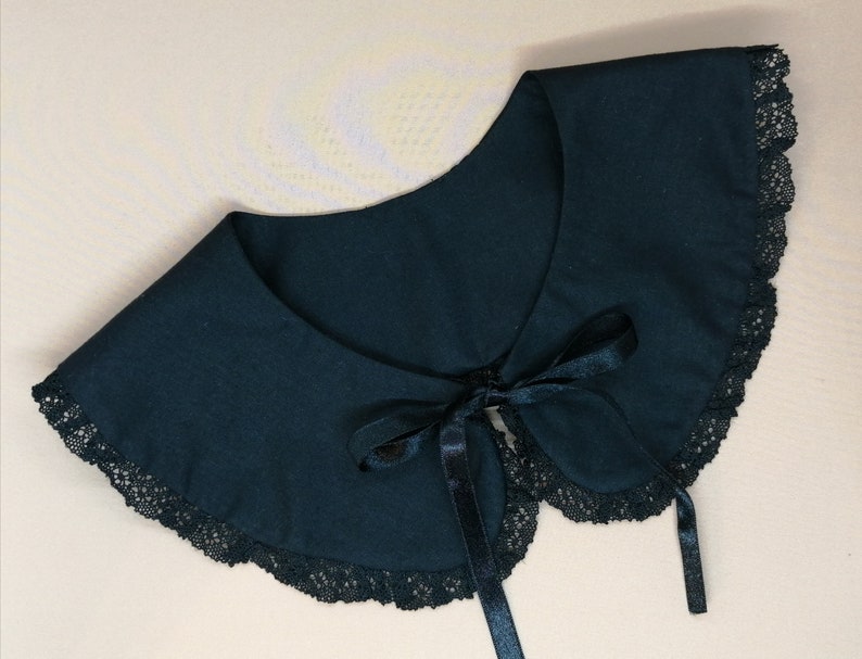 May include: A black lace collar with a black satin ribbon tie. The collar is made of a soft fabric and has a delicate lace trim.