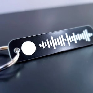 Pode incluir: Um chaveiro de metal preto com um c&oacute;digo Spotify branco e um anel prateado.