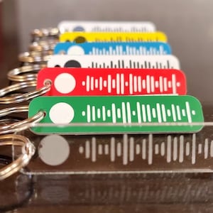 May include: A set of colourful keychains with a white barcode design. The keychains are made of acrylic and have a silver metal ring. The keychains are arranged in a row, with the red keychain at the front and the clear keychain at the back.
