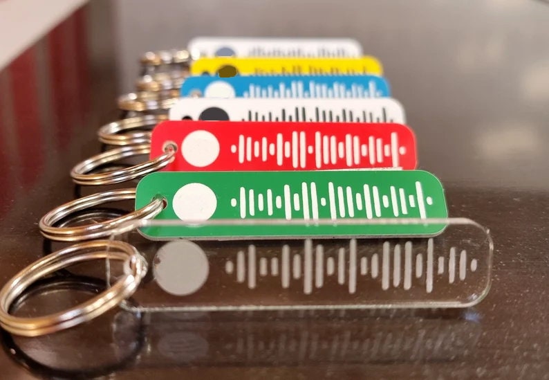 Pode incluir: Um conjunto de chaveiros coloridos com um design de c&oacute;digo de barras branco. Os chaveiros s&atilde;o feitos de acr&iacute;lico e t&ecirc;m um anel de metal prateado. Os chaveiros est&atilde;o dispostos em uma fila, com o chaveiro vermelho na frente e o chaveiro transparente atr&aacute;s.