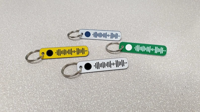 Pode incluir: Quatro chaveiros com fundos de cores diferentes e um design de c&oacute;digo de barras preto e branco. Os chaveiros s&atilde;o amarelo, verde, branco e azul.