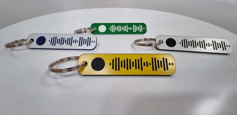 Pode incluir: Quatro chaveiros com fundos de cores diferentes. Cada chaveiro tem um c&iacute;rculo preto e um padr&atilde;o de c&oacute;digo de barras preto e branco. Os chaveiros est&atilde;o sobre uma superf&iacute;cie branca.