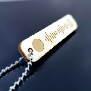 Pode incluir: Um pingente de madeira com uma corrente de prata. O pingente tem formato retangular e apresenta um c&oacute;digo Spotify gravado a laser.