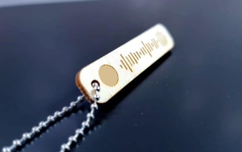 Pode incluir: Um pingente de madeira com uma corrente de prata. O pingente tem formato retangular e apresenta um c&oacute;digo Spotify gravado a laser.