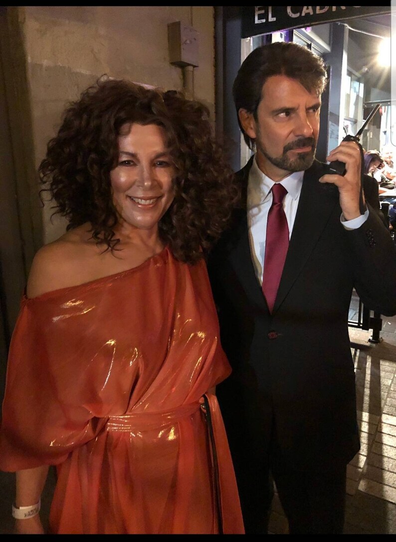 May include: A woman in a bright orange dress with a man in a black suit and a red tie. The man is holding a walkie-talkie.