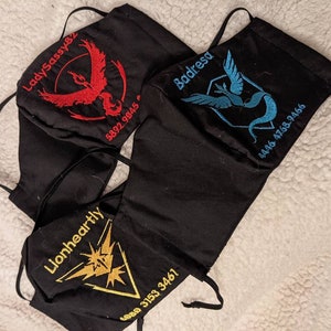 May include: Three black fabric face masks with embroidered Pokemon designs and phone numbers. The masks feature the Pokemon Moltres, Articuno, and Zapdos.