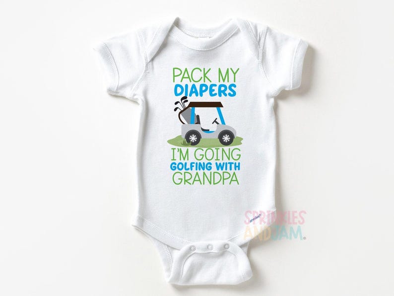 May include: White baby bodysuit with a golf-themed design.  Text reads: 'Pack My Diapers I'm Going Golfing With Grandpa.'  A gray golf cart with green and blue accents is featured in the design. The bodysuit is short-sleeved and has a snap closure.