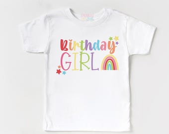 May include: A white short-sleeved t-shirt featuring the multicoloured text Birthday GIRL in a playful font. The design includes small colourful stars and a vibrant rainbow graphic on the right side. The brand name Sprinkles and Jam is printed in small text near the neckline.