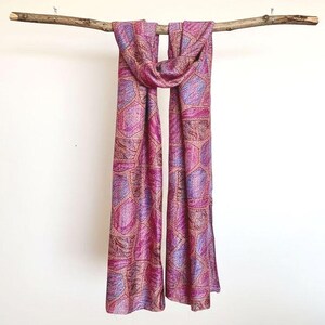 Colourful abstract print pink silk scarf draped over a rustic wooden branch suspended from the ceiling against a plain background