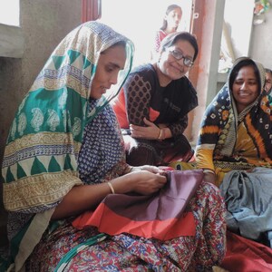Indian Kantha artisans in West Bengal smiling and chatting whilst sewing layers of sari silk with tiny kantha running stitches