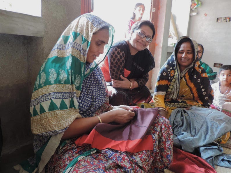 Indian Kantha artisans in West Bengal smiling and chatting whilst sewing layers of sari silk with tiny kantha running stitches