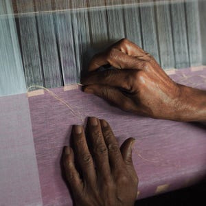 Hands of Indian artisan weaving linen on traditional handloom